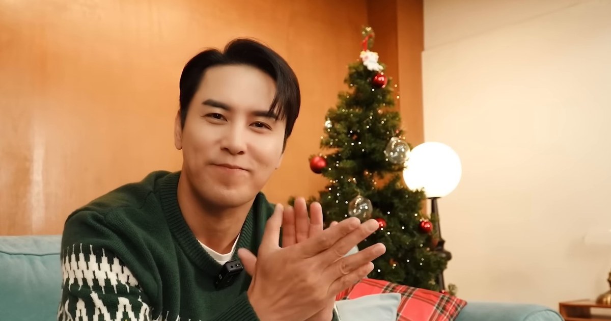 장민호가 초록색 니트 차림으로 크리스마스 트리 앞 소파에 앉아 손뼉을 치며 웃는 모습