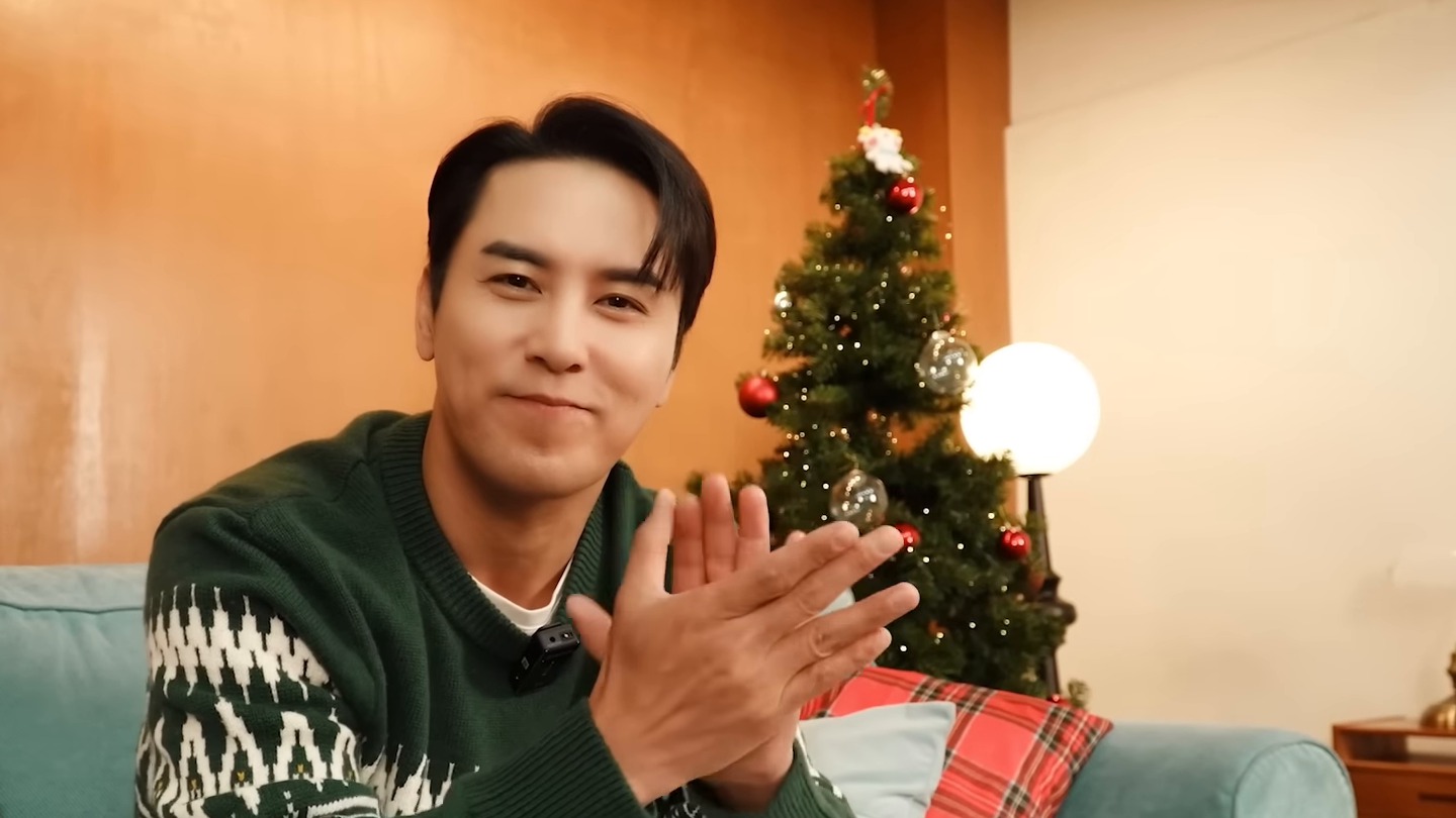 장민호가 초록색 니트 차림으로 크리스마스 트리 앞 소파에 앉아 손뼉을 치며 웃는 모습