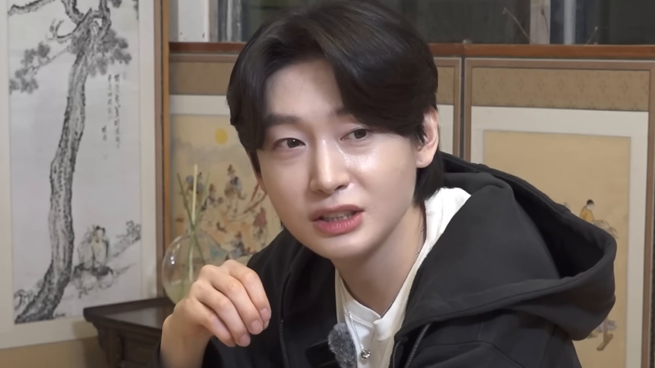검은 후드 차림의 김용빈이 병풍 앞에서 카메라를 보며 이야기하는 모습