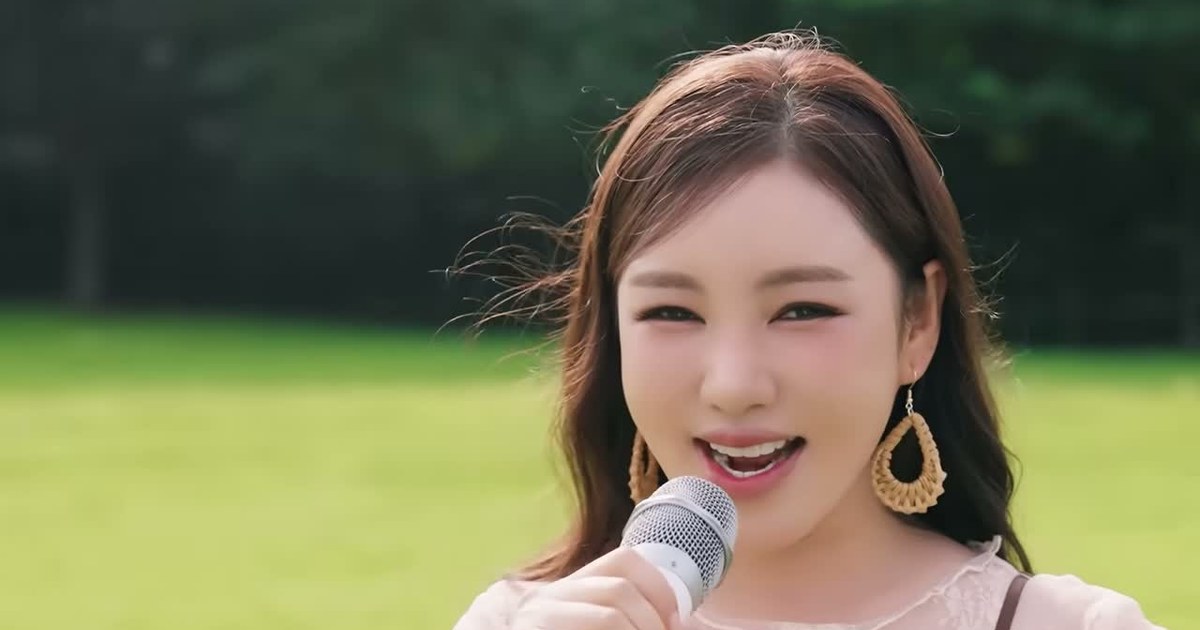 송가인이 초록 잔디밭에서 베이지 블라우스를 입고 마이크를 들고 노래하는 모습