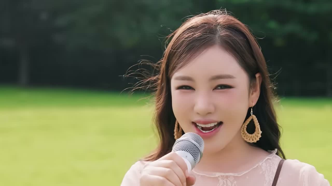 송가인이 초록 잔디밭에서 베이지 블라우스를 입고 마이크를 들고 노래하는 모습