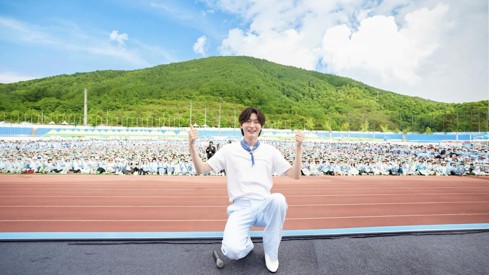 하얀 티셔츠 차림으로 한쪽 무릎을 꿇고 두 엄지를 치켜든 김용빈, 뒤로 운동장 관중석과 푸른 산