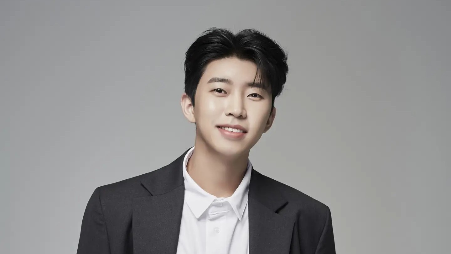 회색 배경 앞에서 짙은 재킷과 흰 셔츠를 입고 웃는 임영웅