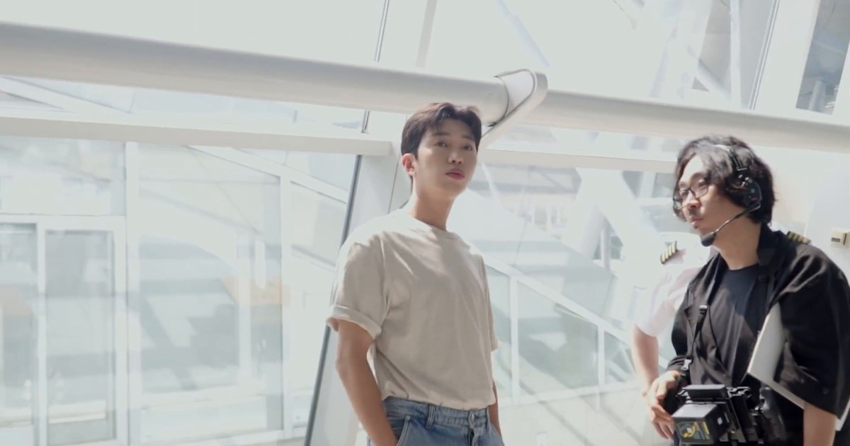 베이지색 티셔츠를 입은 임영웅이 공항 유리 벽 앞에서 스태프와 이야기하는 모습