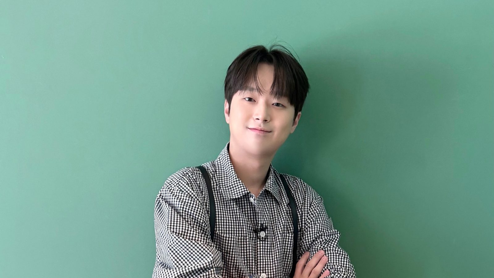 체크무늬 셔츠 차림으로 팔짱을 끼고 초록 벽 앞에서 미소 짓는 이찬원