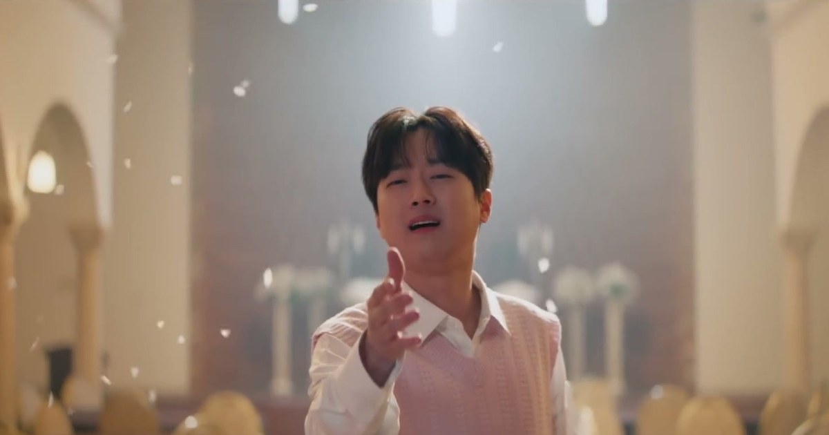 분홍 니트 조끼를 입은 이찬원이 꽃잎이 날리는 홀에서 한 손을 내밀며 노래하는 모습