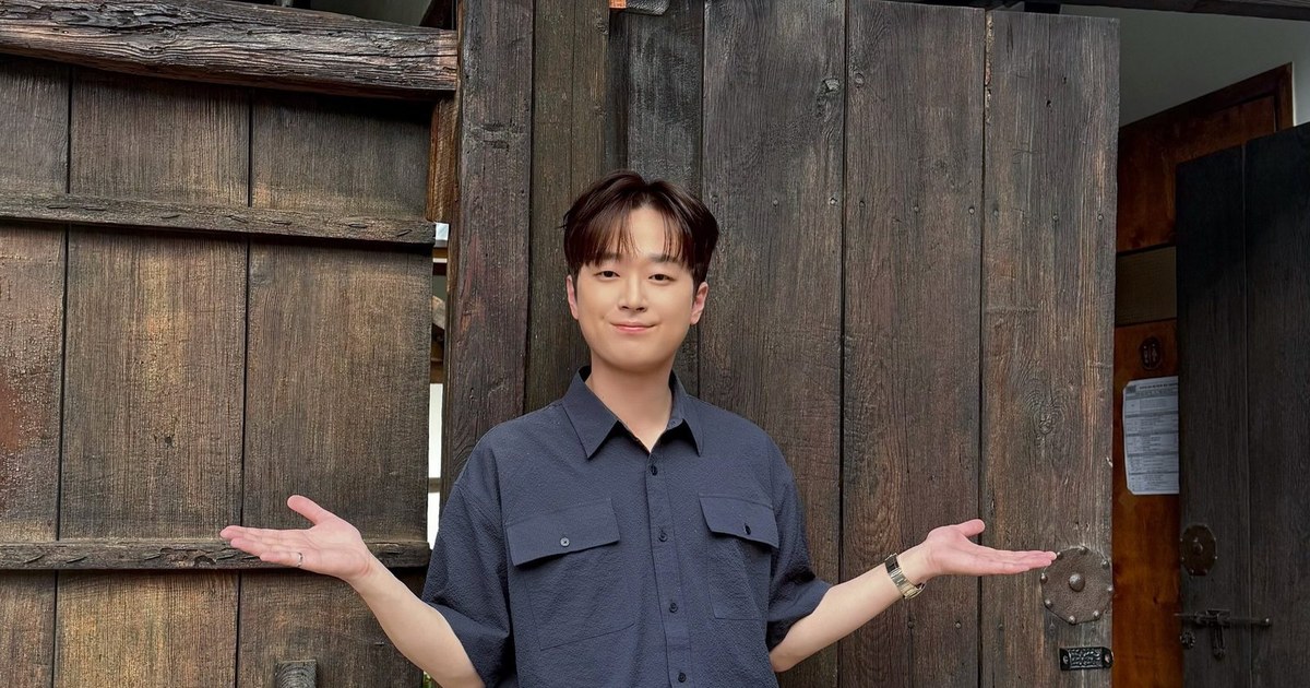 남색 셔츠에 청바지 차림의 이찬원이 오래된 나무 문 앞에서 두 팔을 펼치고 웃는 모습