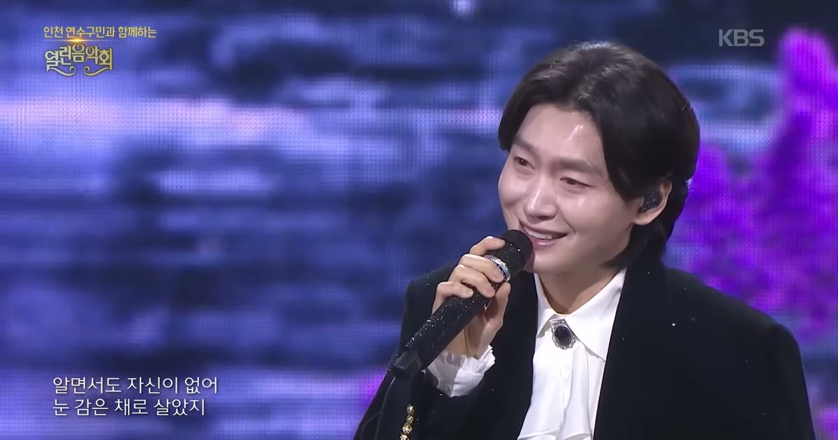검은 벨벳 재킷에 흰 프릴 셔츠 차림으로 마이크를 쥐고 환하게 웃으며 노래하는 김용빈