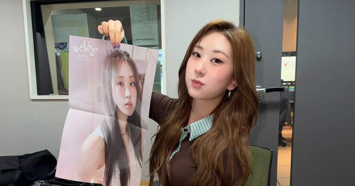 'Adios' 앨범 포스터를 들어 보이며 카메라를 바라보는 전유진